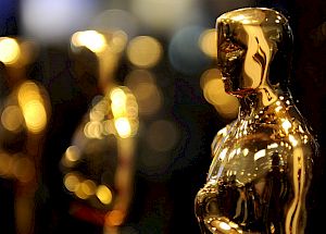 The image shows multiple golden statuettes, commonly known as Oscars, with a blurred background.