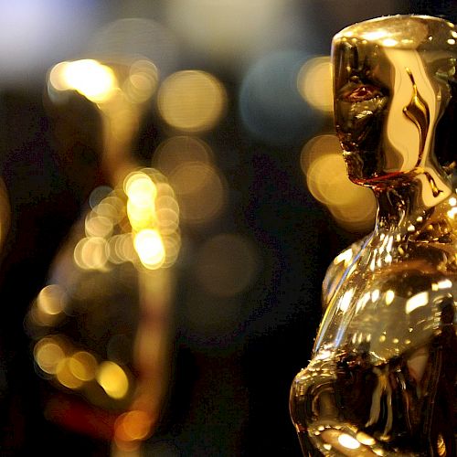 The image shows multiple golden statuettes, commonly known as Oscars, with a blurred background.