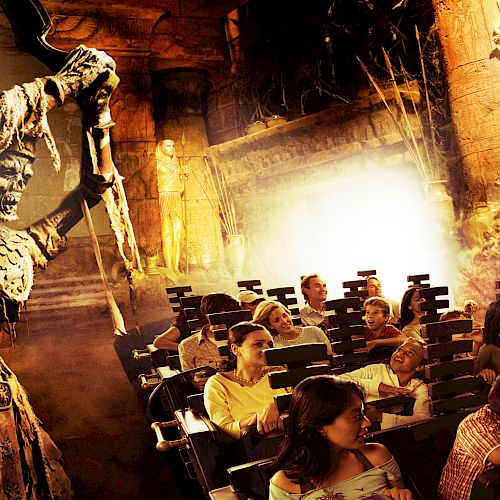 People on an amusement ride with an ancient Egyptian theme, featuring a menacing skeletal figure wielding a staff on the left side.