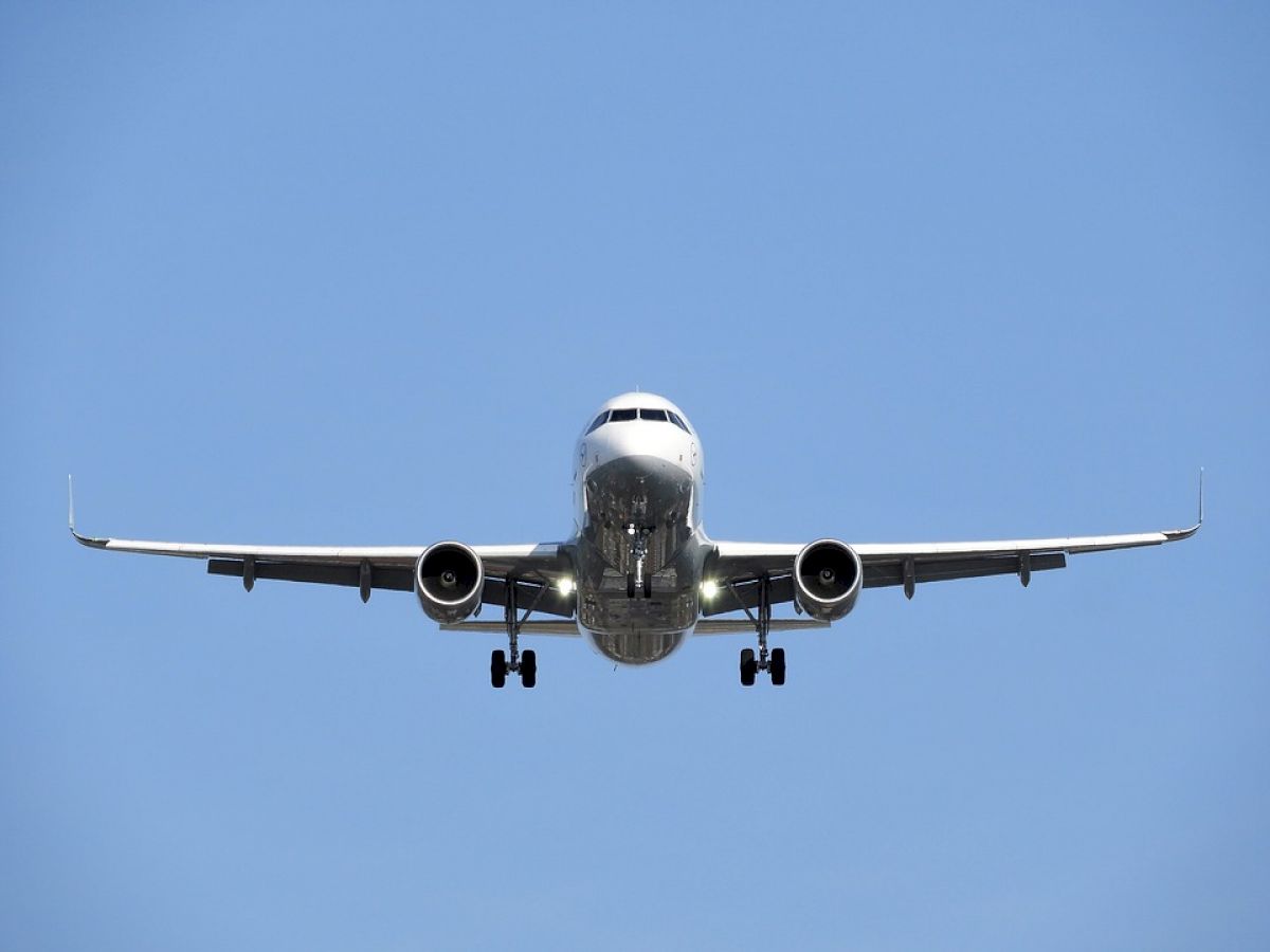 A commercial airplane in flight, seen from the front against a clear blue sky, with its landing gear extended.