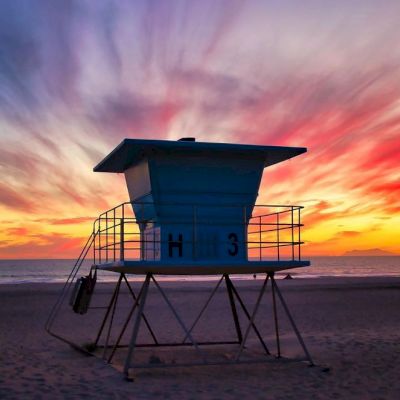 A lifeguard tower stands on a beach at sunset, with vibrant colors in the sky and the ocean in the background.