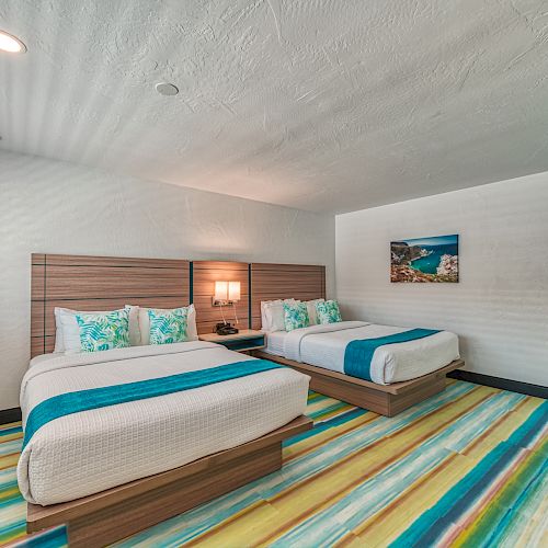 A colorful hotel room with two beds, modern furnishings, and a vibrant striped carpet. There is a photograph on the wall and a vanity area.