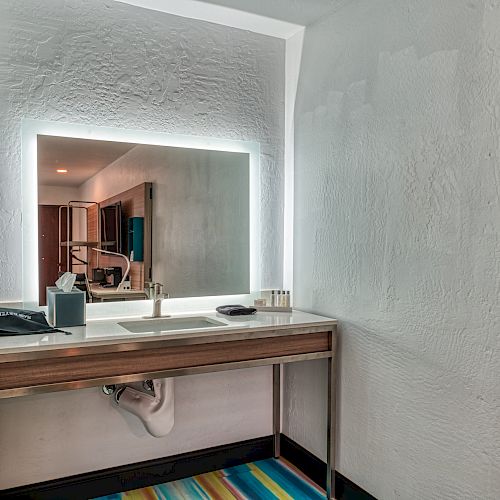 A modern bathroom vanity with an illuminated mirror, a sink, toiletries, and a colorful striped rug in the foreground ends the sentence.