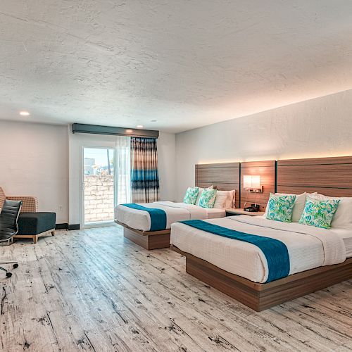 A modern hotel room with two double beds, a desk, and a chair, featuring light wood flooring and contemporary decor.