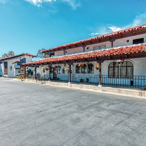 The image shows a two-story building with a red-tiled roof, white walls, and arched windows, resembling a motel or inn on a sunny day.