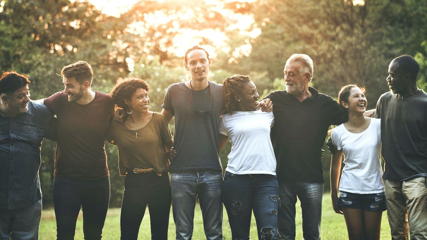 A group of diverse people standing outside in a line with their arms around each other, smiling and enjoying the sunny day.