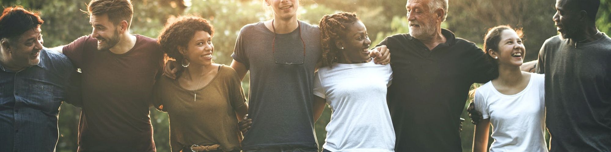 A group of diverse people standing outside in a line with their arms around each other, smiling and enjoying the sunny day.