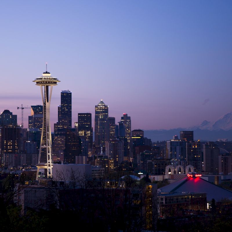 The image shows the Seattle skyline at dusk, featuring the Space Needle prominently and Mount Rainier in the background under a twilight sky.