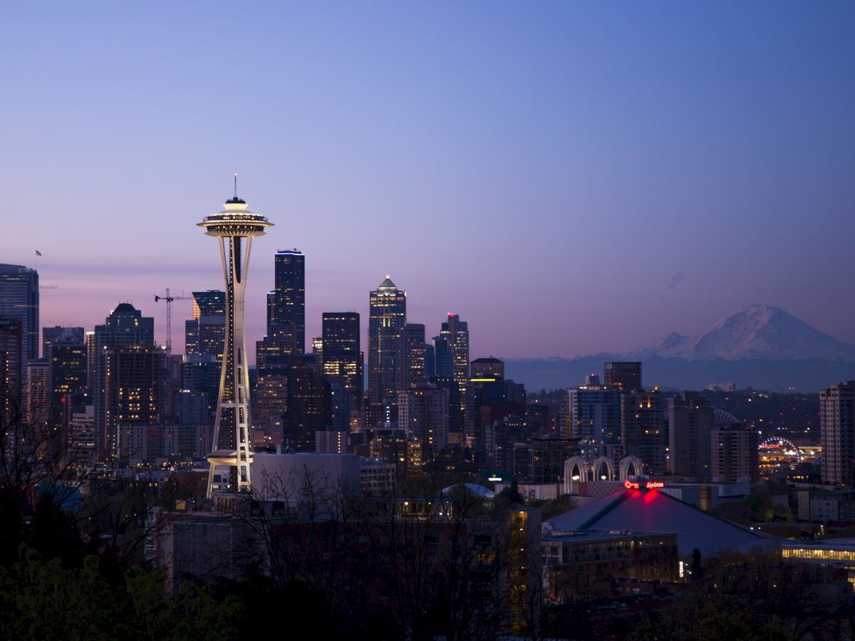 This image features the Seattle skyline at dusk, with the Space Needle prominently visible and Mount Rainier in the background.