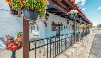 This image shows a picturesque building with arched windows and hanging flower pots under a red-tiled roof, featuring a patio with seating.