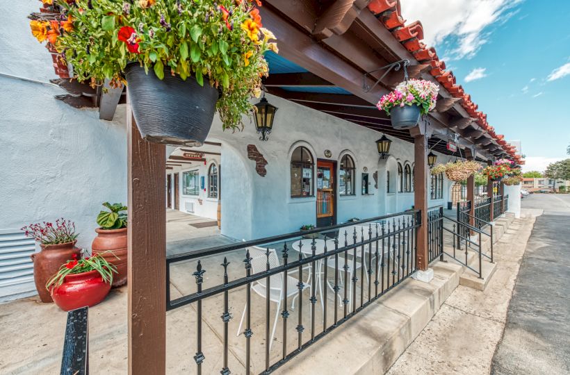 This image shows a picturesque building with arched windows and hanging flower pots under a red-tiled roof, featuring a patio with seating.