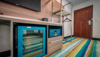 A hotel room entryway with a minibar, safe, television, open closet with hangers, and a colorful striped floor carpet.